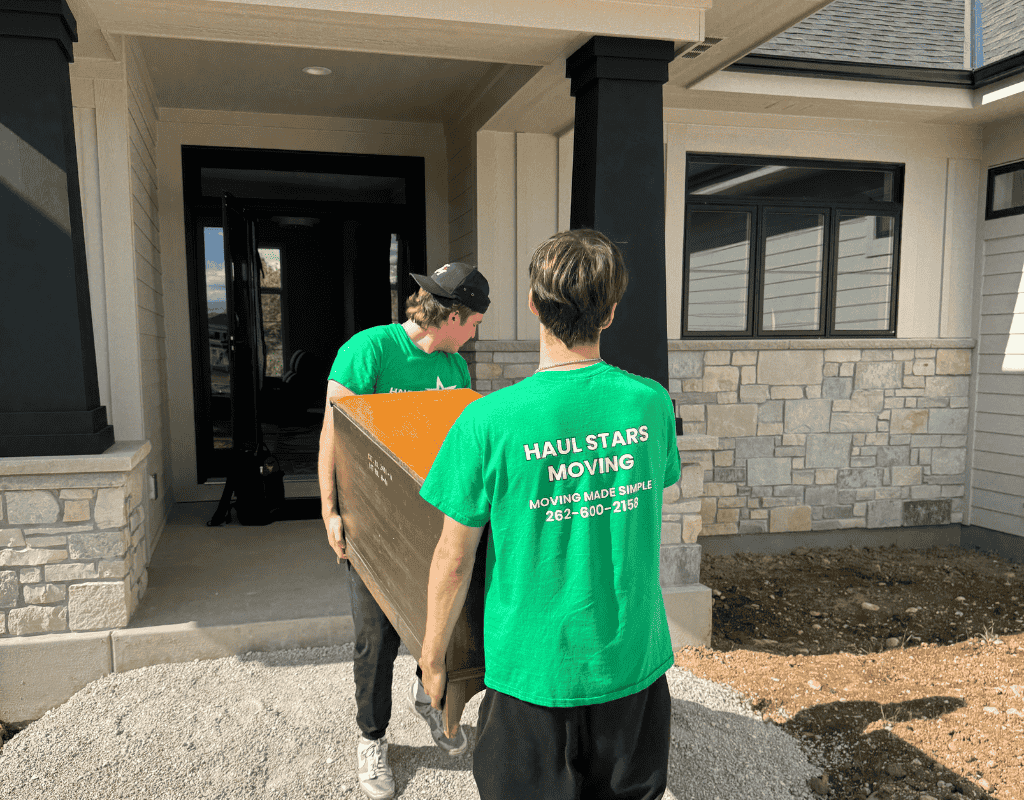 Two movers in Haul Stars Moving shirts carrying a large box out of a suburban condo entrance in Milwaukee