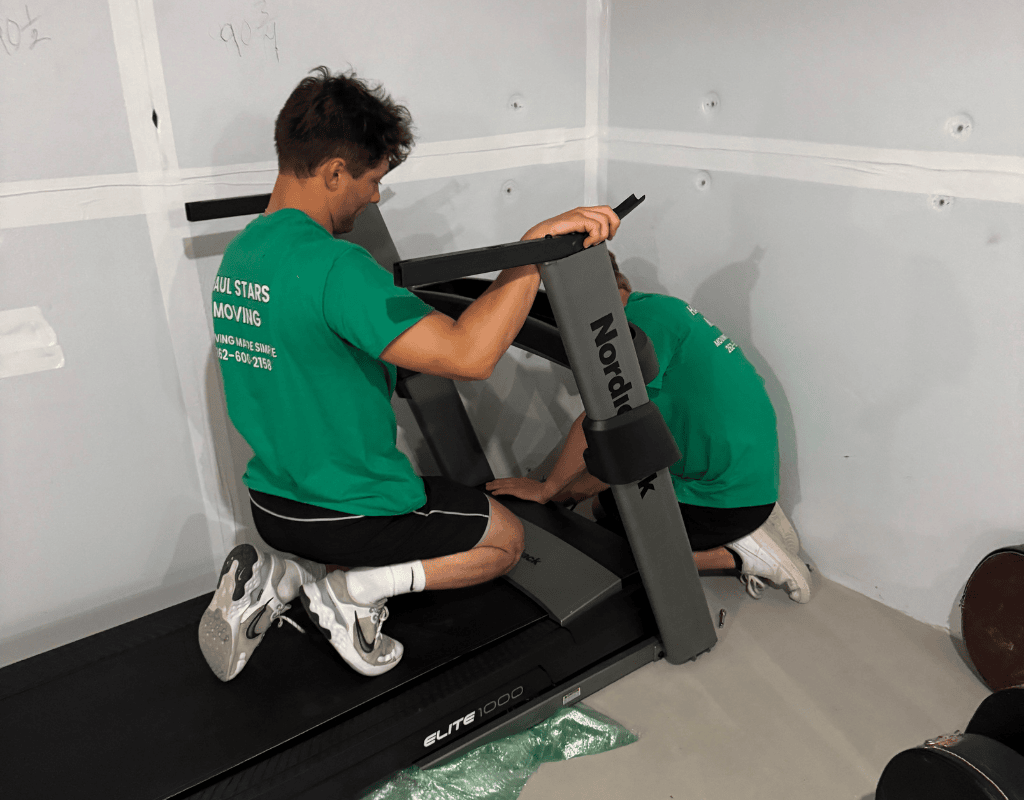 Two Haul Stars movers assembling a treadmill in a Milwaukee apartment as part of condo moving
